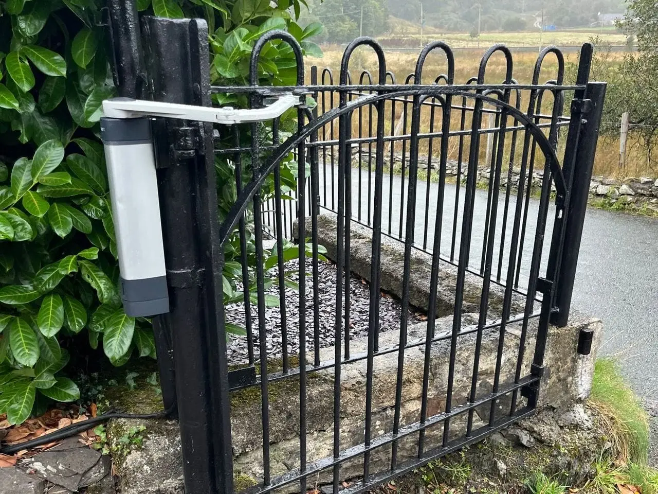 Gate operator arm fitted to a black wrought-iron railing gate