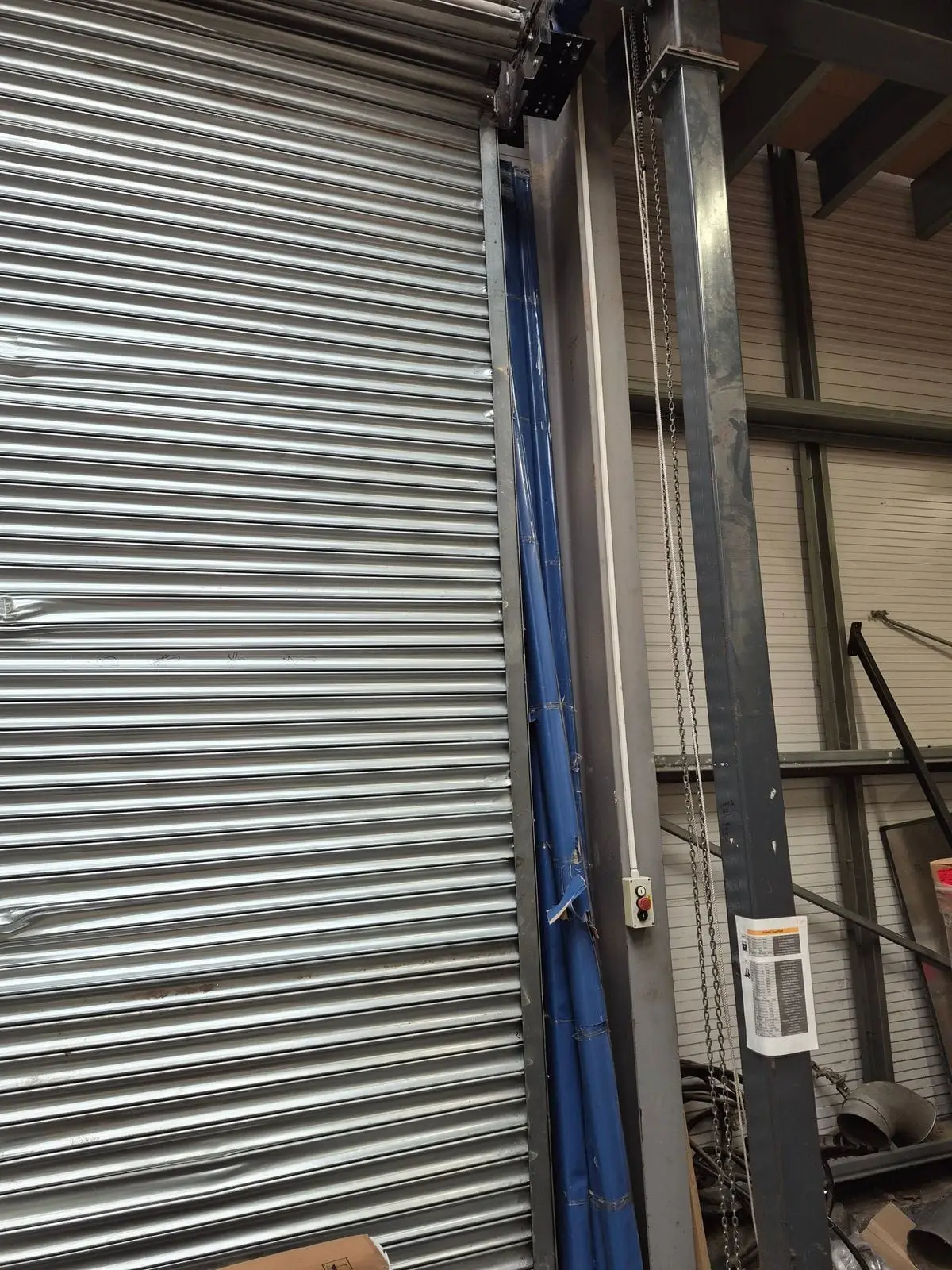 Large silver roller shutter with impact dents inside an industrial unit