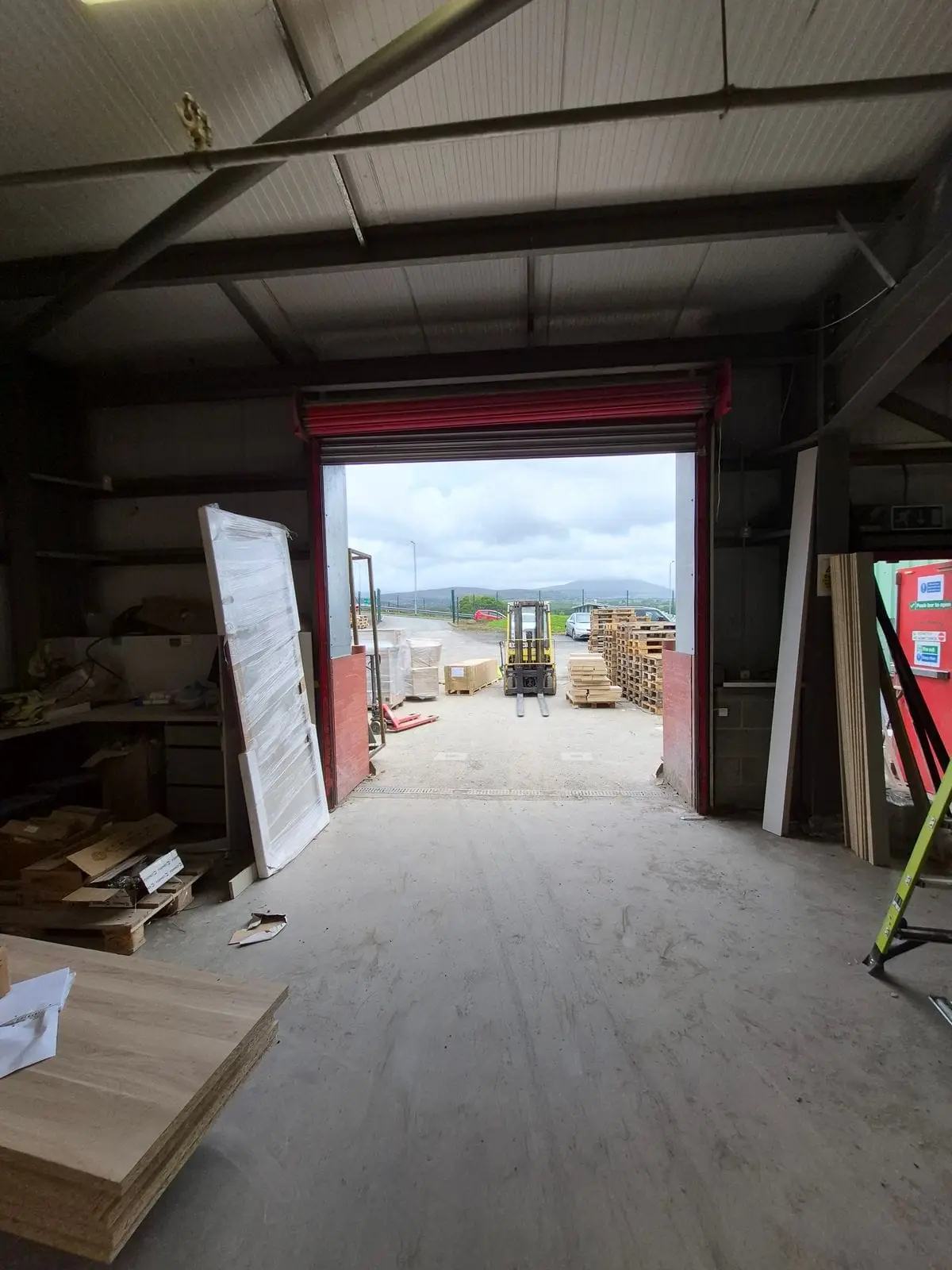 Red roller shutter open to a yard, seen from inside a workshop