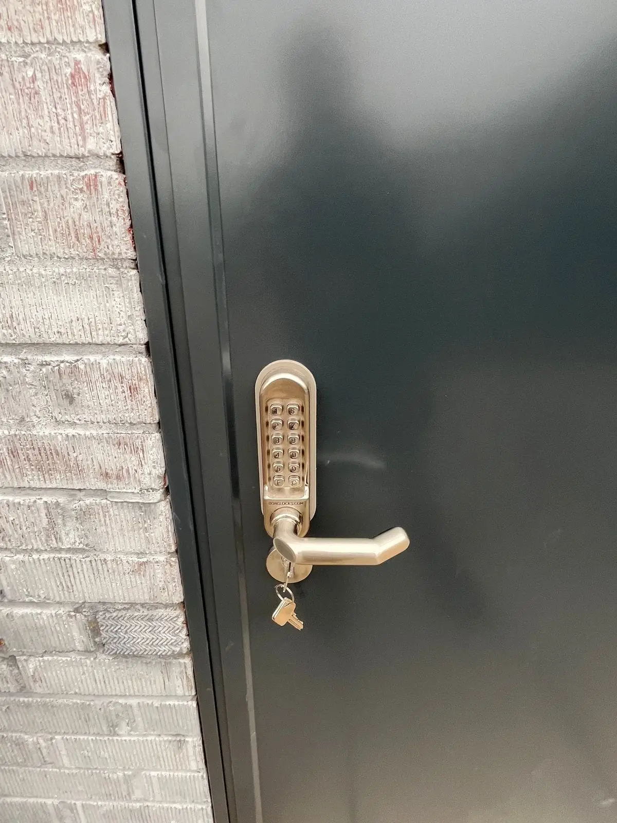 New dark grey steel door with a push-button code lock beside painted brick