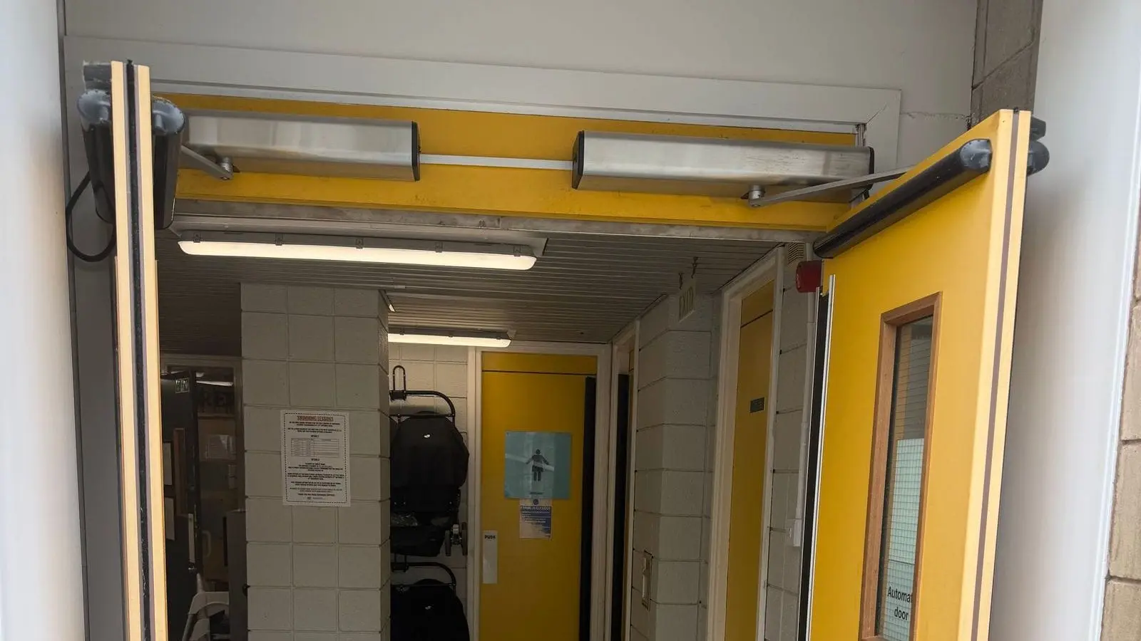Yellow swing door with an automatic operator and automatic door sign in a corridor